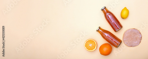 Horizontal banner with two bottles of kombucha tea, scoby and citrus fruits for additional flavors on yellow pastel background with copy space. Orange, lemon. Healthy fermented drink. Flatlay mockup