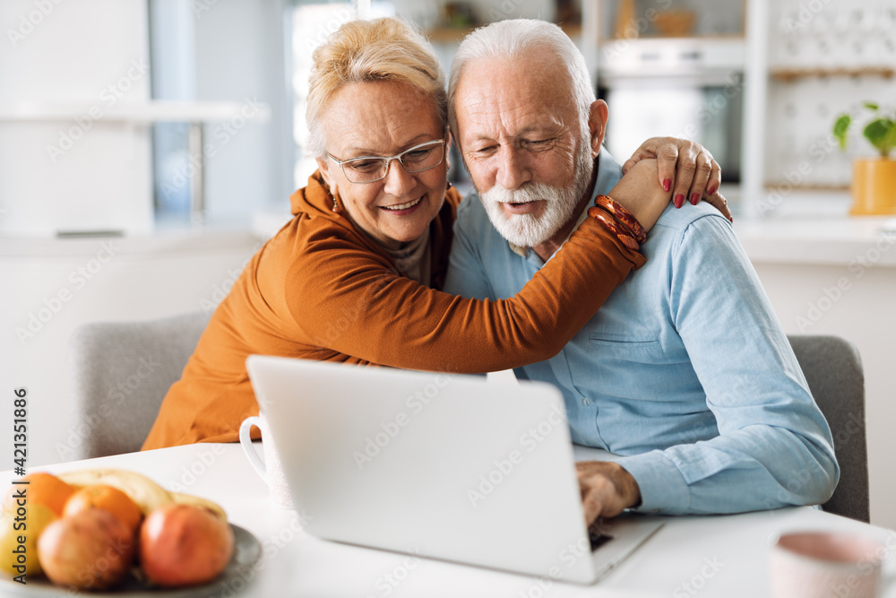 Embraced mature couple surfing the Internet on laptop at home Embraced mature couple surfing the Internet on laptop at home