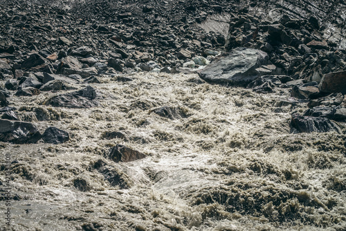 Scenic highlands landscape of powerful mountain river beginning from glacier among large moraines. Beautiful scenery with glacier at source of turbulent river. Mountain river source among big stones.