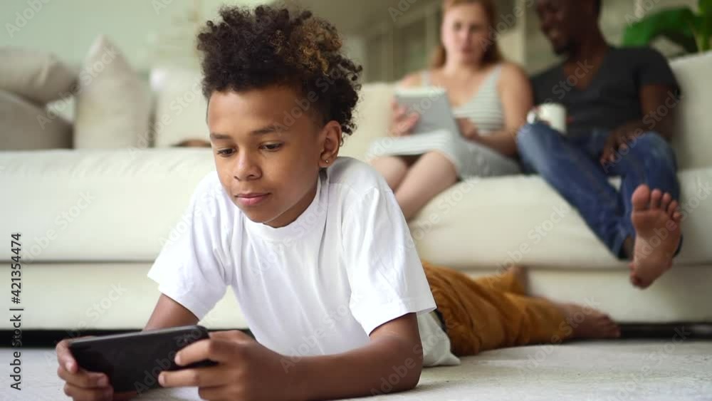 Child boy play games on phone on floor and his parents use tablet on sofa. Spbd Addicted mixed race Child boy play games on phone on floor and his parents use tablet on sofa. Spbd Addicted mixed race