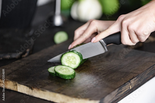 woman hand cutting cucumber on chopping wood