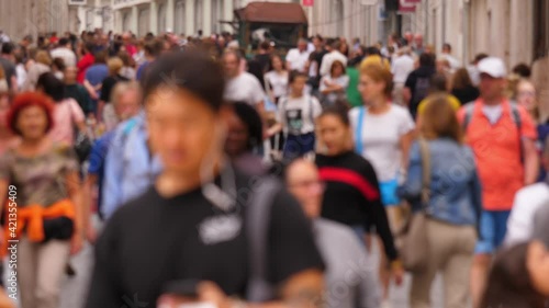 Blurred view of crowded pedestrian street at Lisbon downtown. Many people walk at inclined road. Popular shopping and touristic area of city, Rua do Carmo at bustling at summer day