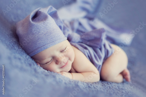 Newborn baby sleeps on blanket. Time to sleep for infant. Tiny baby with leprechaun cap and wrap lies on the soft violet blanket.