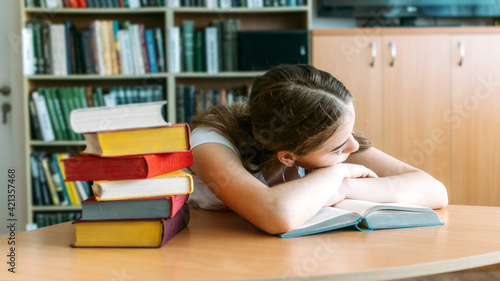 College Students overwhelmed, overworked, burned out, perfectionists. Teen tired girl, young woman sitting at table with books in college library photo