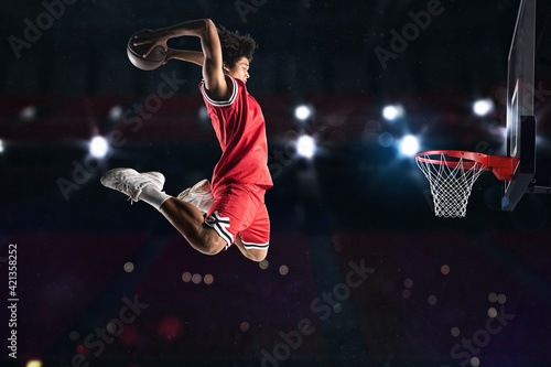 Foto Basketball player in red uniform jumping high to make a slam dunk to the basket