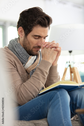 young man praying on wooden bible at home