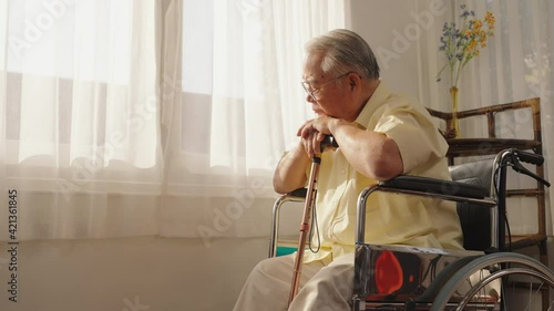 Portrait depressed lonely elderly man with wooden cane looking at windows, frustrated mature male folded hands on walking stick, sitting on wheelchair alone, loneliness and solitude, Care, Retirement.