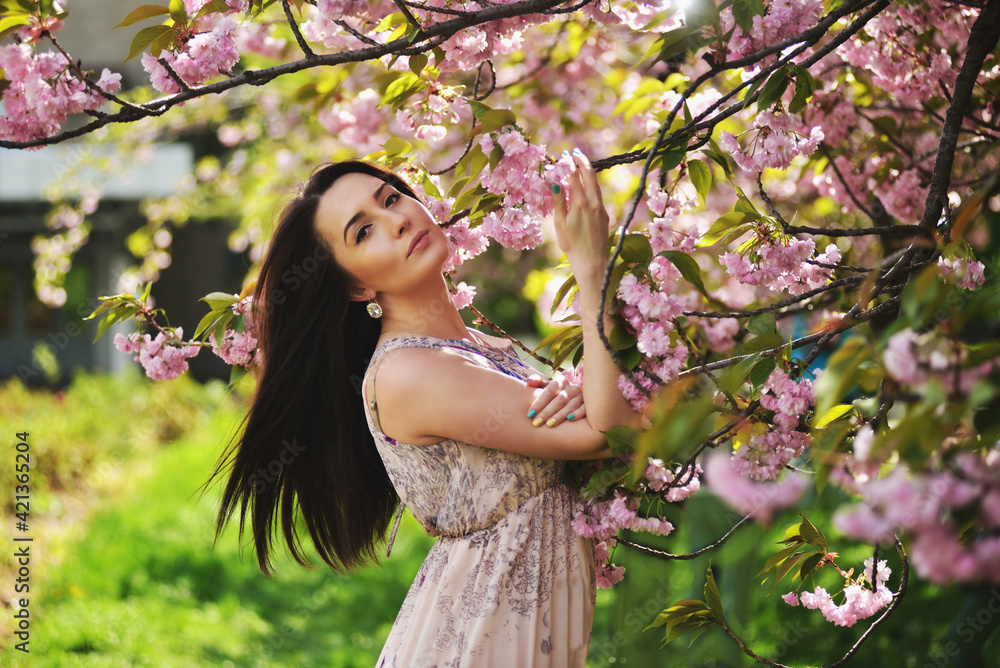 Young woman with long hair posing near sakura tree in a garden. Spring day. Spring pink sakura blossom. Perfume and fashion Young woman with long hair posing near sakura tree in a garden. Spring day. Spring pink sakura blossom. Perfume and fashion