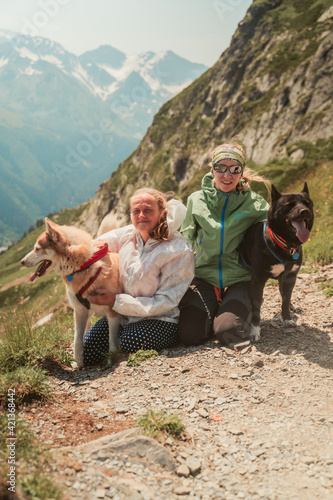 Two women with dogs on a hike. Mountain landscape, two huskies and two people. Travel portrait. The greatness of nature. Happiness and gratitude for the opportunity to live.