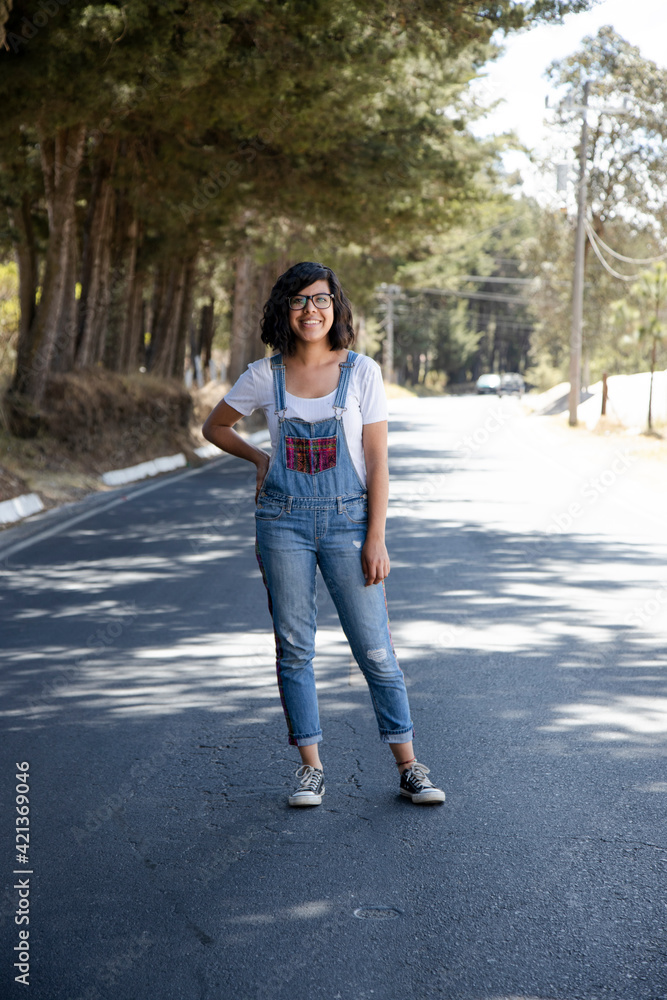 Young Hispanic woman smiling stopping in the middle of the road - lonely woman enjoying the road trip