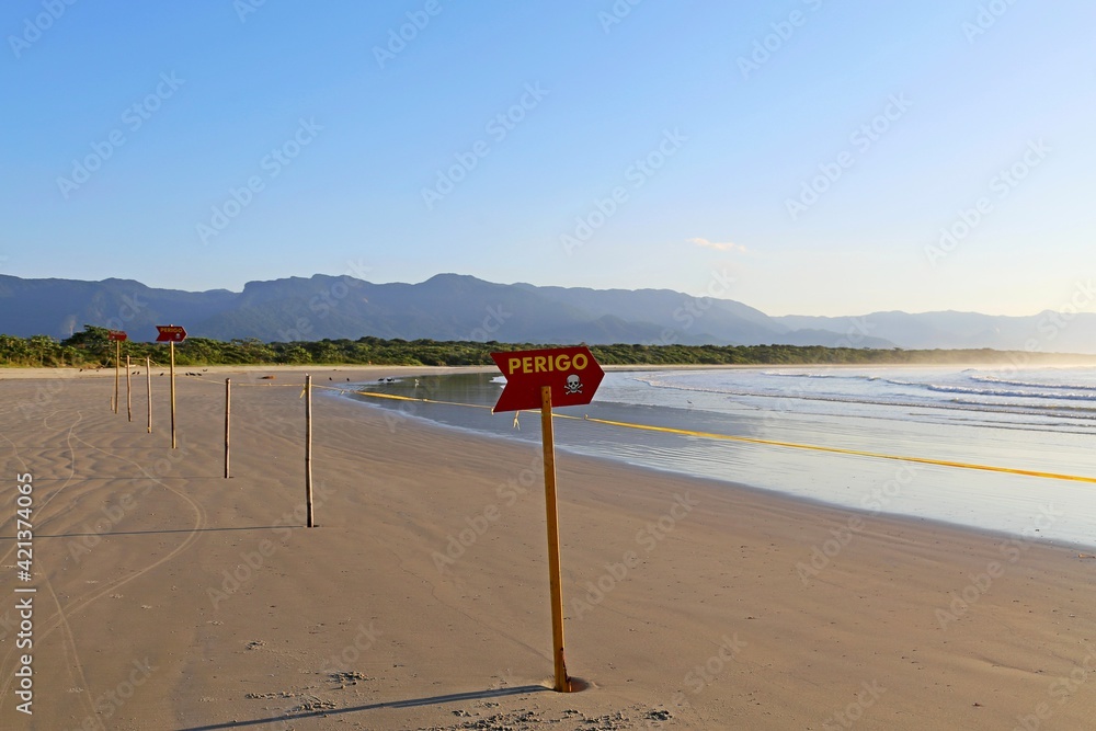 Beautiful empty beach with a red sign with word danger. Calm, waters, sand and vegetation in the background.