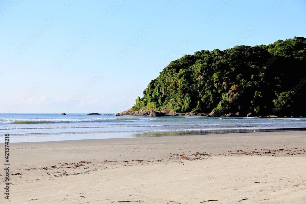 Seascape with beach sand, calm waters, sea, and one island with tropical vegetation.