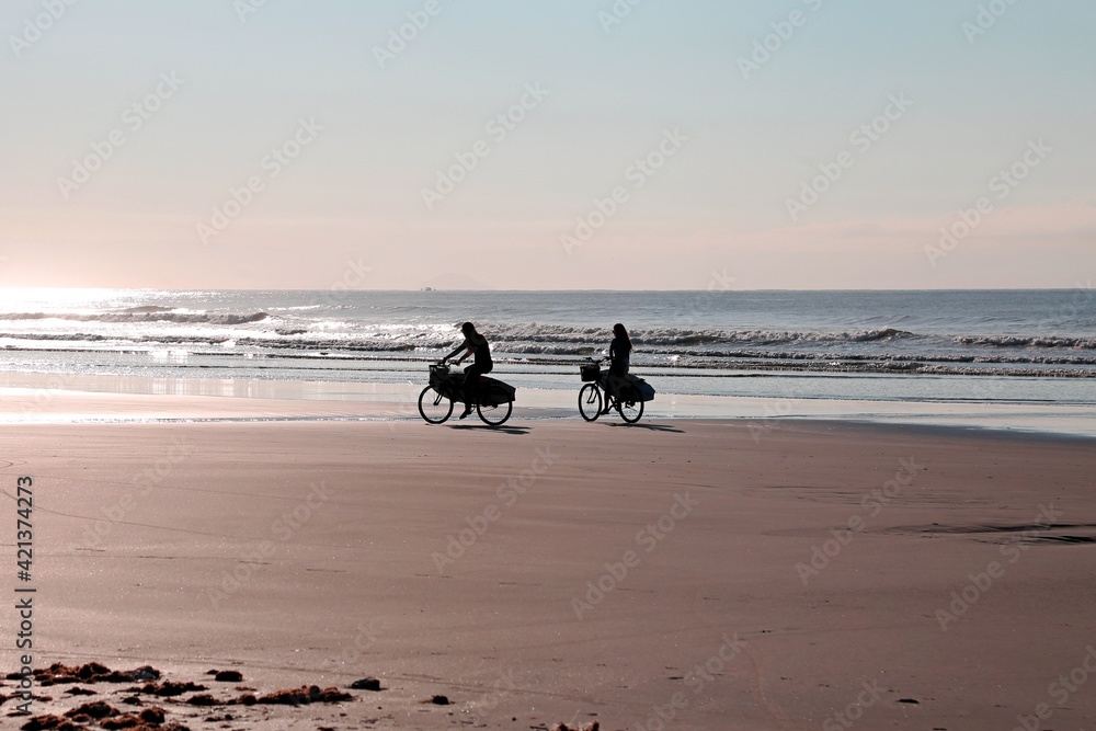Two girls on their bikes with surfboard by the sand on the beach. Two girls on their bikes with surfboard by the sand on the beach.