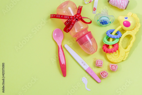 Pregnancy test and accessories.Pregnancy test and baby accessories lie on the right on a yellow pastel background with space for text on the left, top view, close-up.