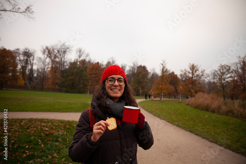 woman wearing a red hat, drinking from a red cup, forest background in autumn