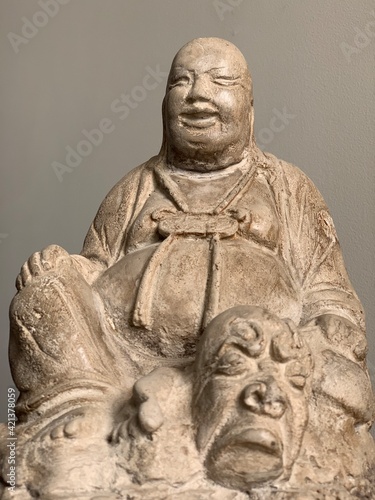 Antique laughing Buddha statue, sitting above a devil face. Laughing Buddha is a symbol of wealth and happiness