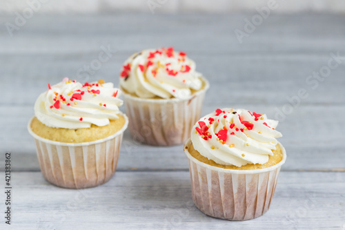 Three cupcakes with white cream sprinkled with hearts.
