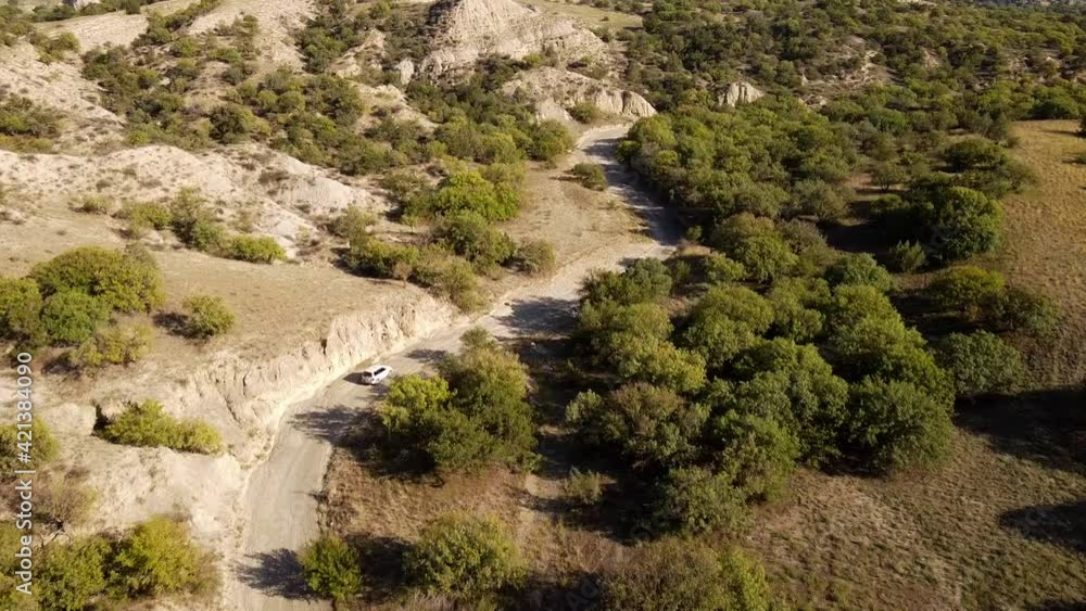 Aerial drone push in shot of an offroad car driving on a dirt road in the middle of a desert, mountains behind, in Vashlovani National Park, Georgia Aerial drone push in shot of an offroad car driving on a dirt road in the middle of a desert, mountains behind, in Vashlovani National Park, Georgia