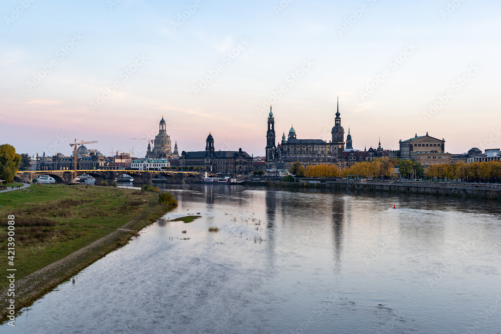 Dresden urban skyline at Elbe River in autumn season. Beautiful colorful leaves at sunset evening. Reflections in the water of this landscape. Construction site at an old bridge.