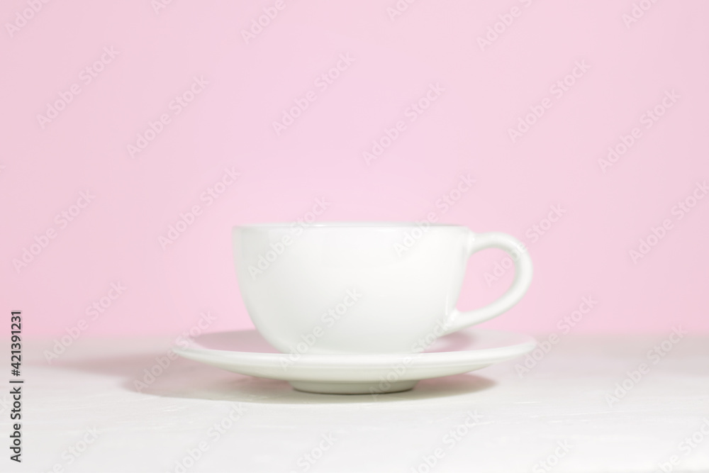 White mug with tea or coffee on a saucer, on a concrete table, on a pink background. Hard shadows. White mug with tea or coffee on a saucer, on a concrete table, on a pink background. Hard shadows.