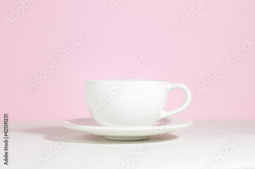 White mug with tea or coffee on a saucer, on a concrete table, on a pink background. Hard shadows.