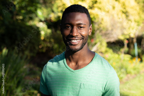 Portrait of african american man looking at camera and smiling on sunny garden terrace
