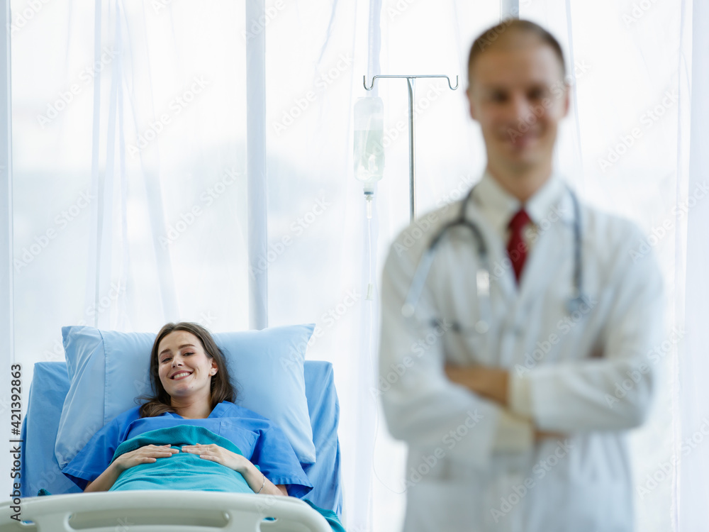 Obraz premium Focus to caucasian woman patient smiling look at camera and sleep on bed in room. Doctor man wearing uniform carrying stethoscope on neck smiling and standing folded crossed arms