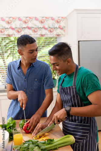 Diverse gay male couple spending time in kitchen cooking together and smiling