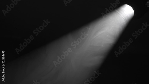 This video shows smoke moving through a spotlight beam of light in a dark, black environment.