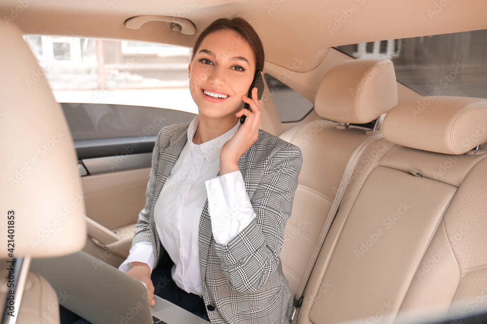 Young businesswoman talking by phone on backseat of car