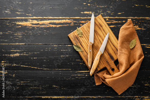 Board with knives and bay leaves on dark wooden background