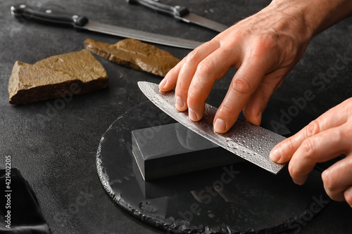 Man sharpening knife on dark background photo