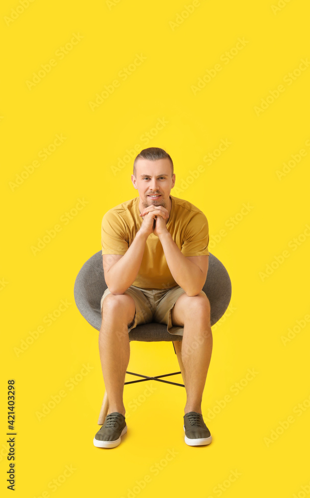 Young man sitting in armchair on color background