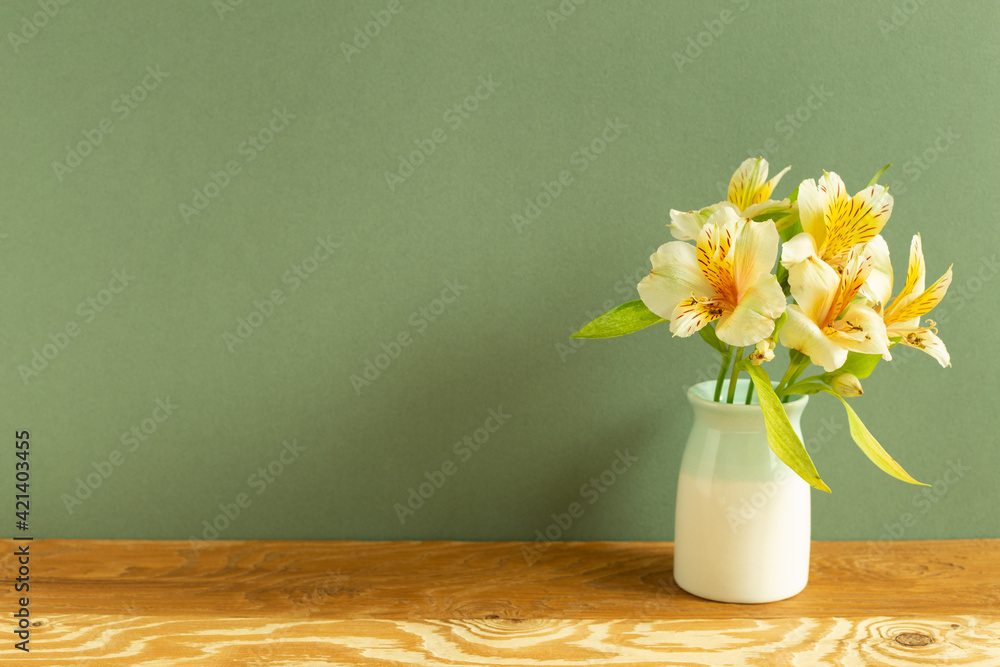 Vase of yellow alstroemeria flowers on wooden table. green background. home interior
