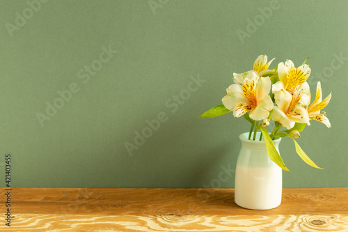 Vase of yellow alstroemeria flowers on wooden table. green background. home interior photo