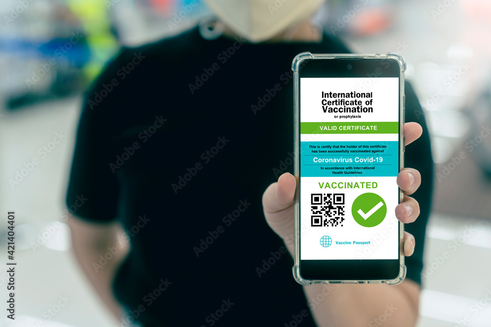 asian female show Smartphone displaying a valid digital vaccination certificate passport for COVID-19 in male's hand, public area background. Vaccination, disease immunity passpor