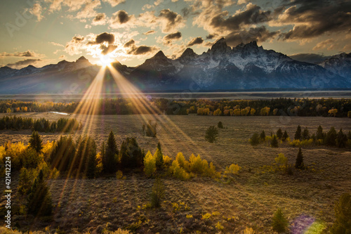 dramatic sunset in the snow capped peaks of the Grand Teton Mountain range and vibrant autumn colors of the trees in Jackson Hole ,Wyoming.