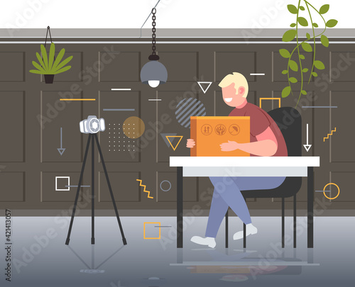 man blogger opening parcel box recording unboxing video with camera on tripod blogging mail delivery concept office interior horizontal full length