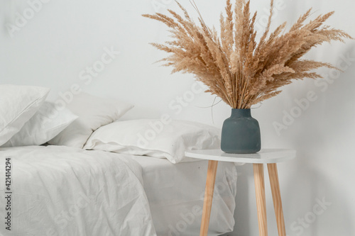 White minimalistic bedroom in Scandinavian and Boho style. Pampas grass in a bouquet in a vase on the bedside table photo