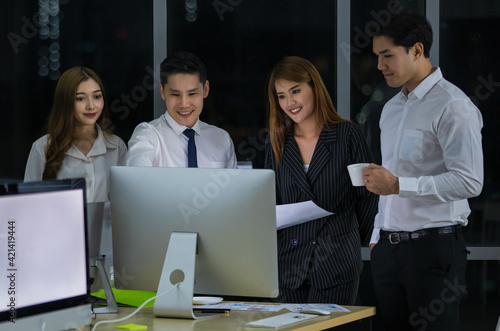 Professional young adult Asian businessman leader consulting and explaining their current project plan to concentrated colleagues that gathered in front of computer while sitting at office at night