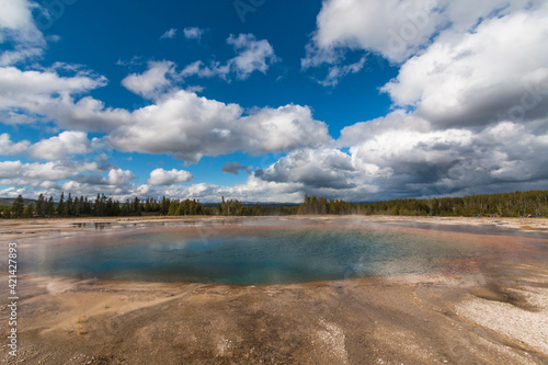 dramatic landscape of a hot spring overcast by large cotton like clouds in the Midway Geyser basin in Yellowstone in Wyoming.