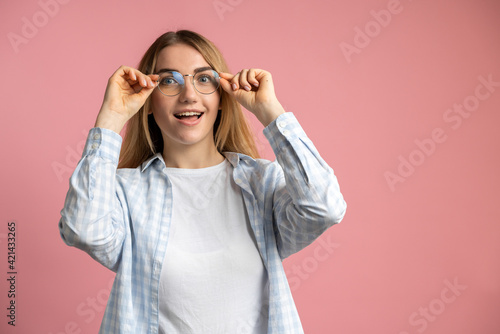 A young, beautiful blonde on a pink background put on glasses and began to see better. The concept of health care, taking care of one's own life.