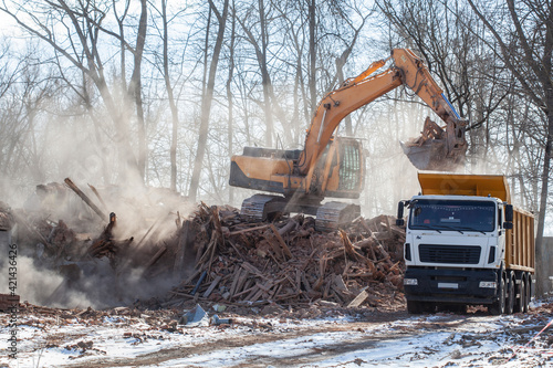 excavator loading a dump truck with debris and trash after building demolition
