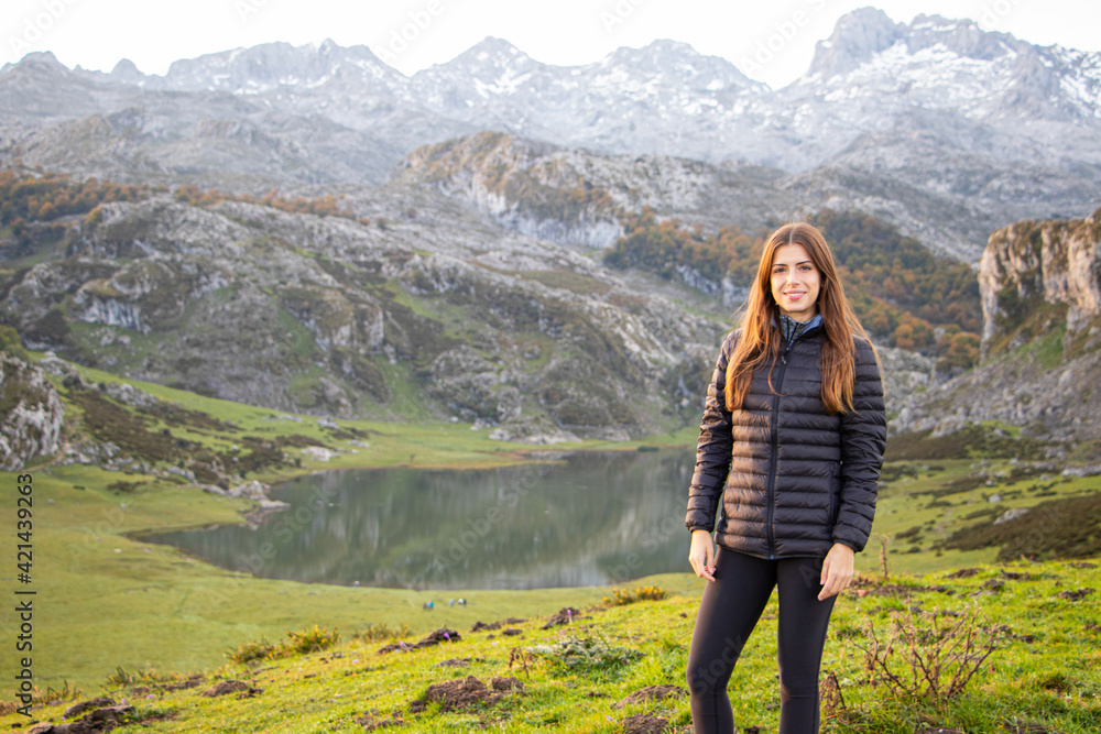 GIRL STANDING NEXT TO A LAKE WITH A BEAUTIFUL LANDSCAPE FULL OF MOUNTAINS. NATURE AND PEOPLE CONCEPT. COVADONGA, SPAIN.