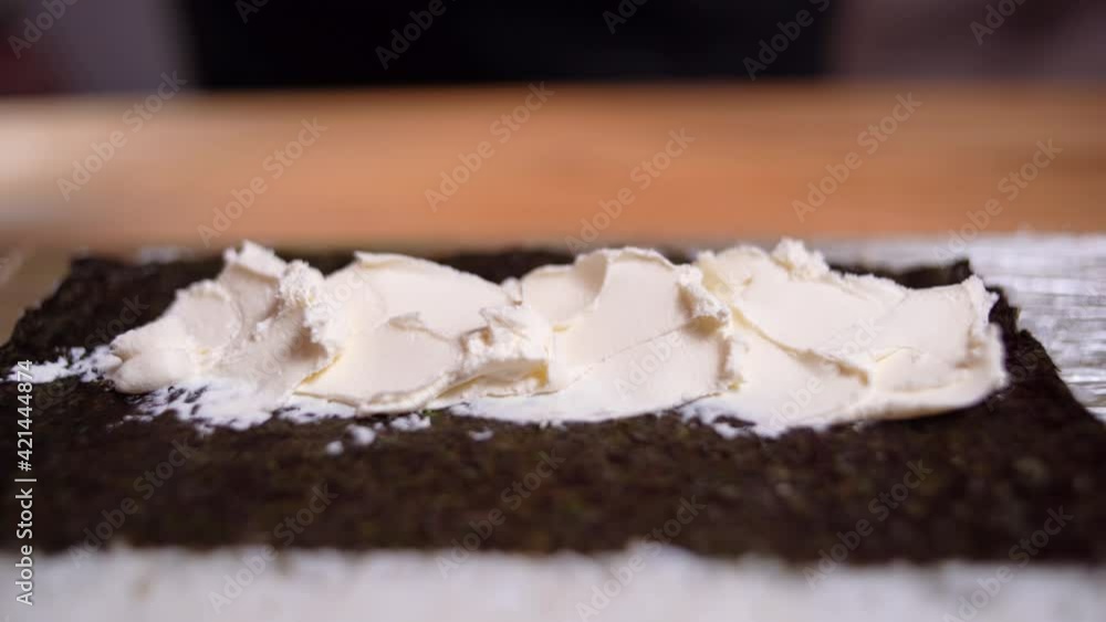 Close scene of cooking process. Chef is doing a sushi rolls. He is squeezing the cream cheese from the confectionery bag on nori and then put the cucumber near. Close scene of cooking process. Chef is doing a sushi rolls. He is squeezing the cream cheese from the confectionery bag on nori and then put the cucumber near.