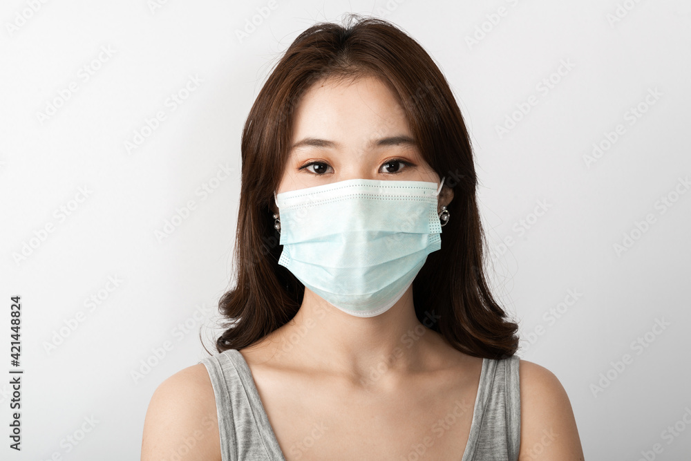 Close-up front view of A beautiful young Asian girl is wearing a face mask to protect the pollution or covid19 virus disease. White background in the studio. Healthcare and virus pandemic concept Close-up front view of A beautiful young Asian girl is wearing a face mask to protect the pollution or covid19 virus disease. White background in the studio. Healthcare and virus pandemic concept