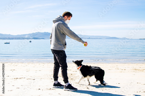 man in medical mask playing with his dog on the beach in the new normal