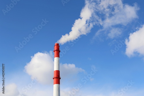 Factory chimney on blue sky and clouds background with white smoke. Concept of steam plant, air pollution, heating season