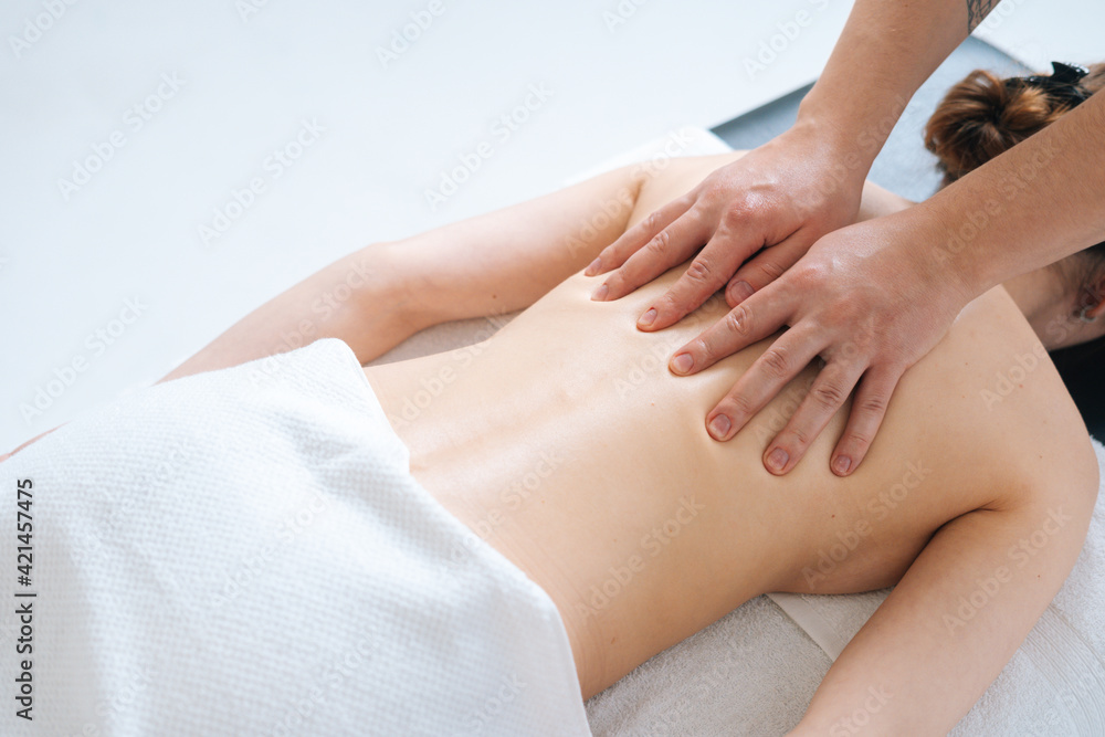 Top close-up view of male masseur massaging back and shoulder blades of female lying on massage table at spa salon. Beautiful young woman with perfect skin getting relaxing massage.