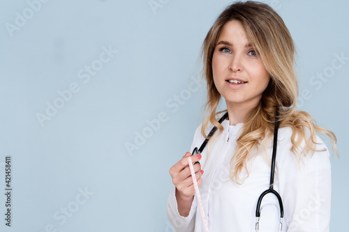 beautiful woman doctor dietologist in white coat with stethoscope and centimeter measuring tape isolated on gray background